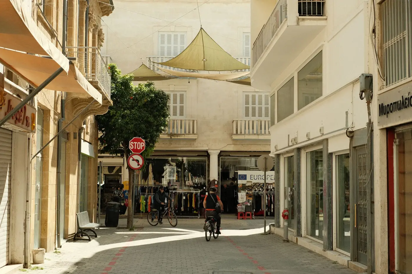 A pedestrianised shopping street with Greek signage and shade sails strung between the buildings