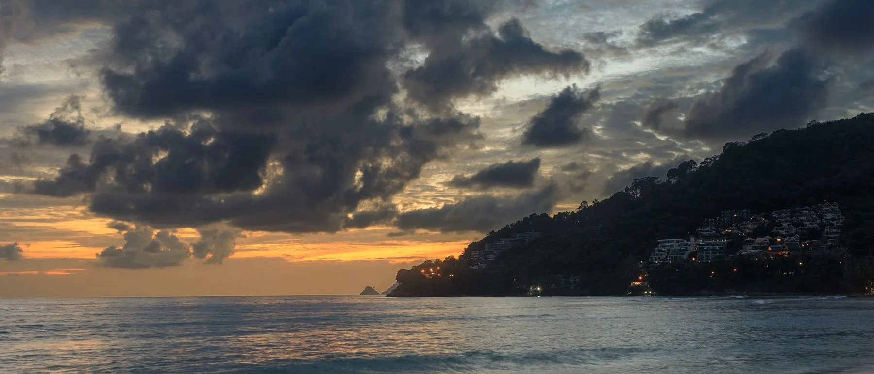 Evening light over a Thai coastal bay with hillside residences above the water